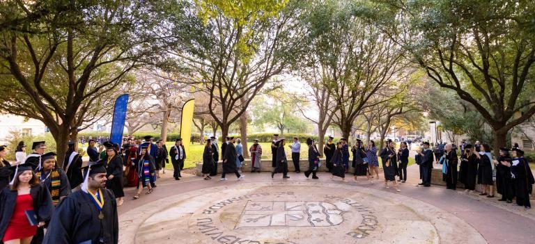 Graduates wear caps and gowns and walk around the university seal during the Legacy Walk.