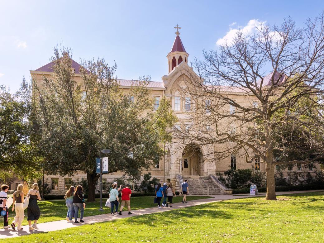 A group of people walk on a pathway in front of Holy Cross Hall.