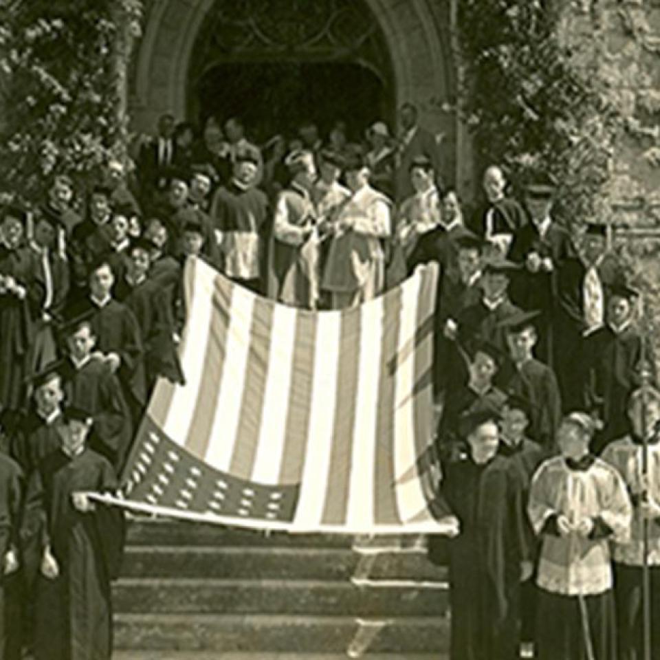 St. 爱德华的 students and Holy Cross Brothers stand in front of the school with an American flag in the 1920s