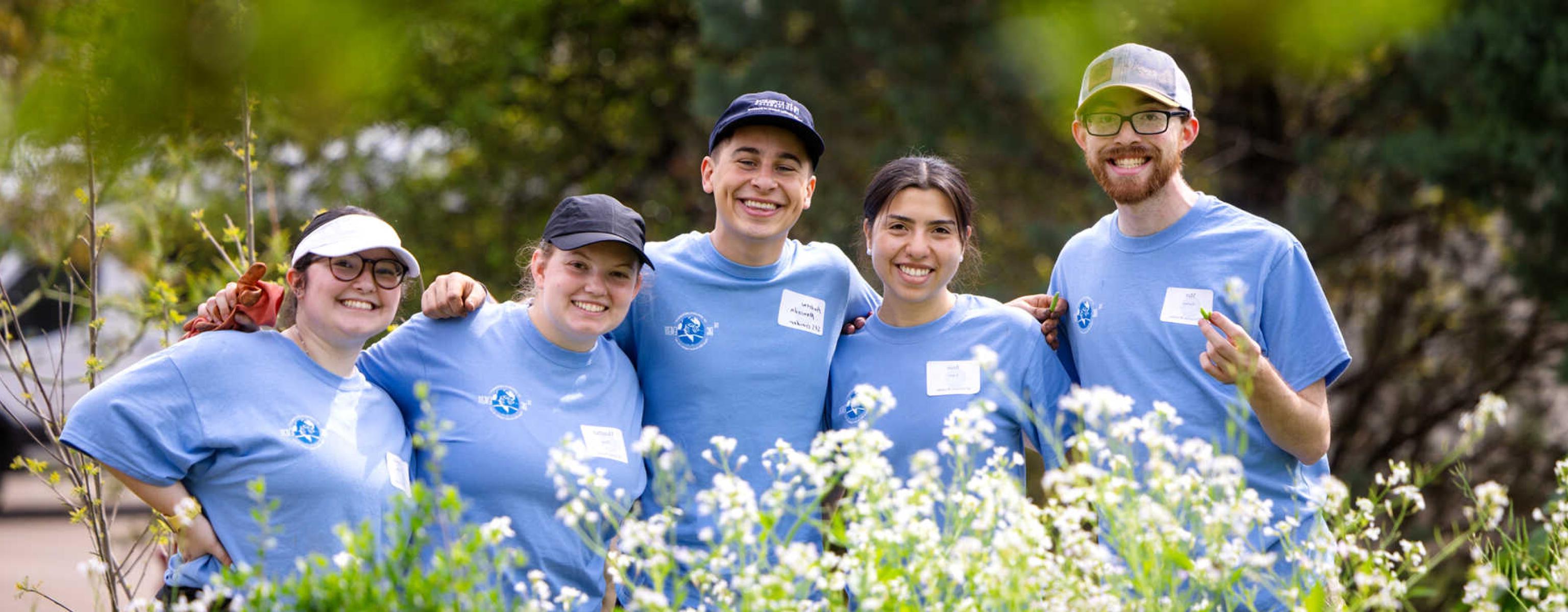 Five students wearing matching blue Big Event shirts are framed by foliage.