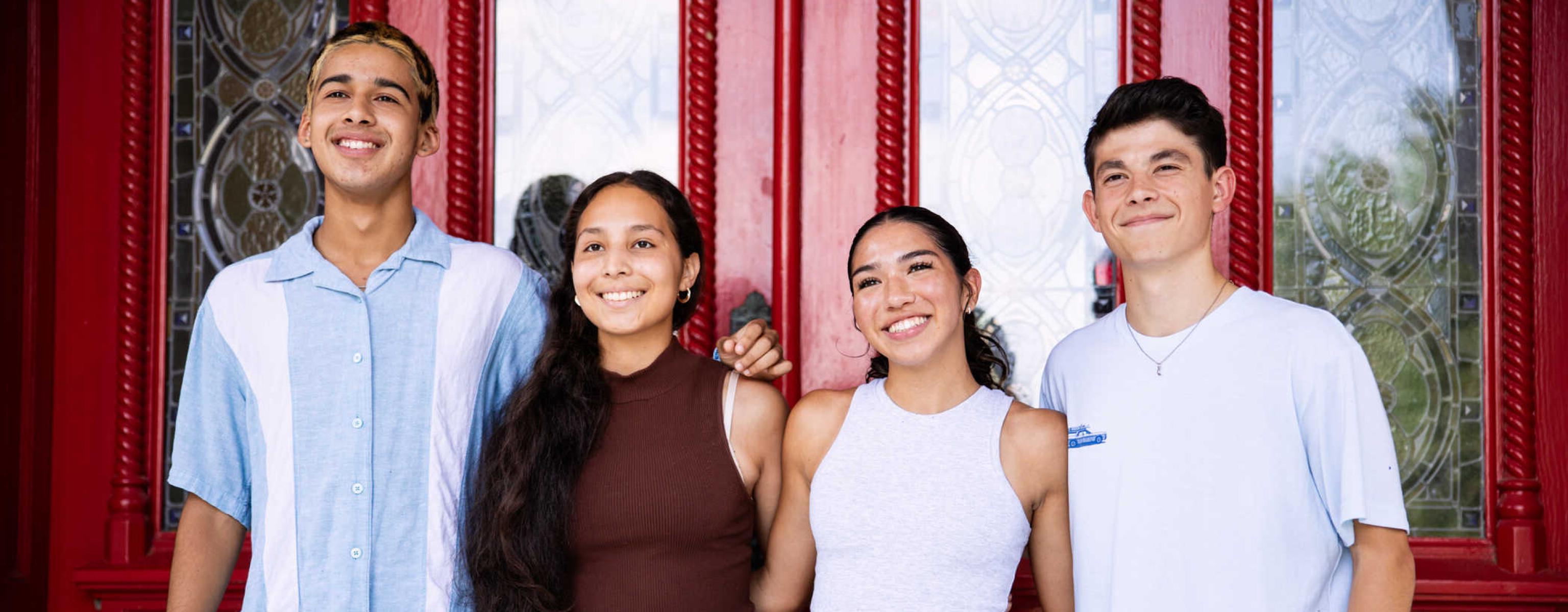 Four students stand together for a group photo at Main Building's red doors after orientation.