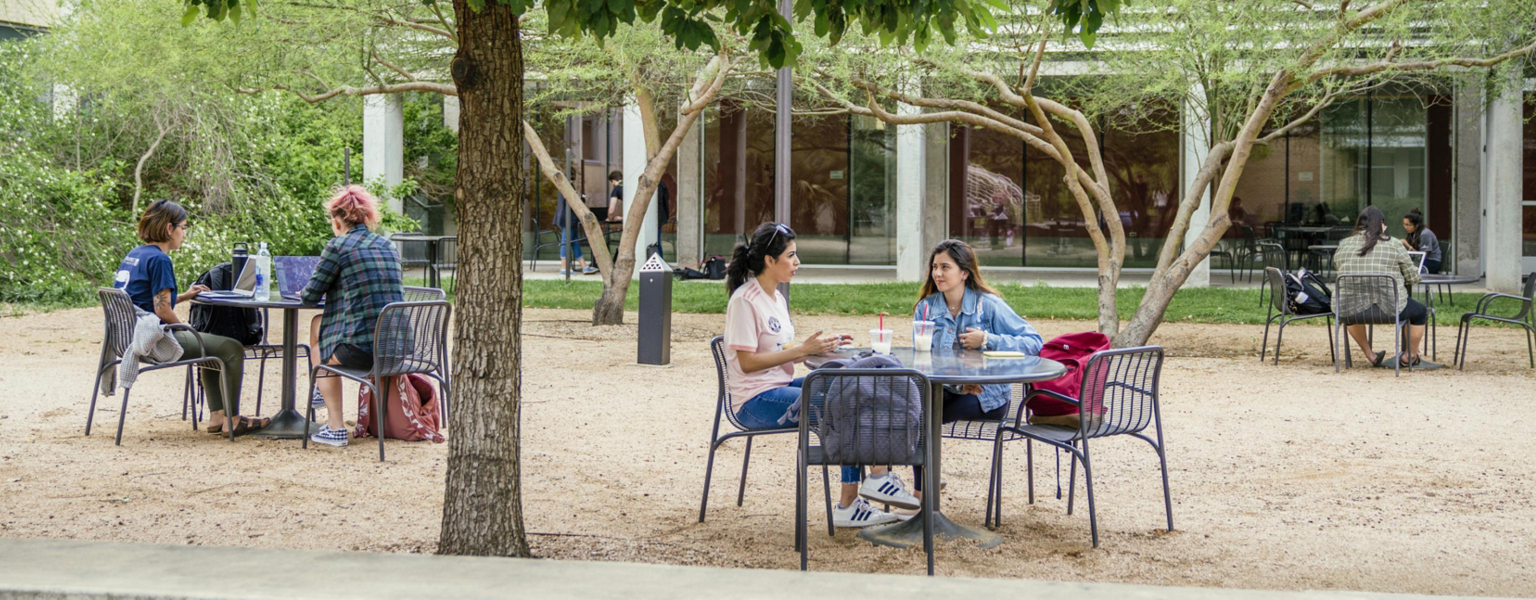 Students sit at tables in the Equity Hall courtyard, with backpacks and laptops, hanging out with friends and studying.