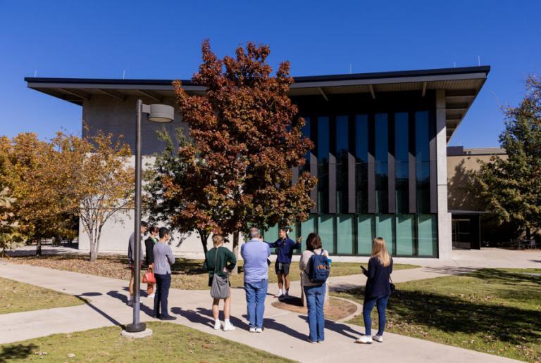 A campus tour guide leads a tour and chats with prospective students and families on a path outside Munday Library.