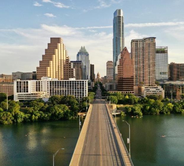 Aerial view of a road bridge over water leading to downtown Austin with tall buildings in the background.