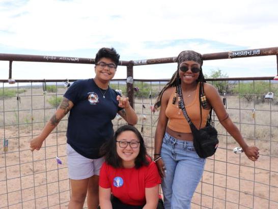 Three students throwing the "Toppers Up" in front of a fence in the desert