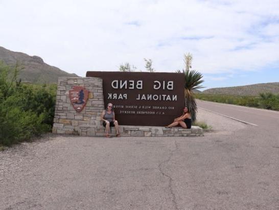 Two students sitting in front of a large sign that reads "Big Bend National Park"