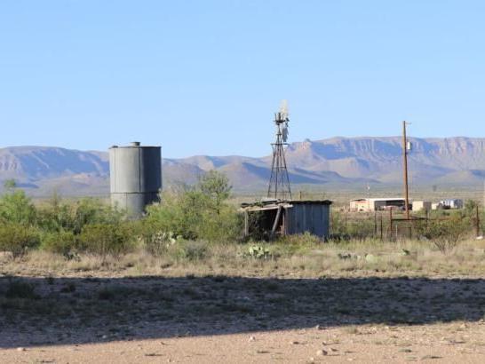 A desert scene with shrubs, distant mountains, and a metal windmill