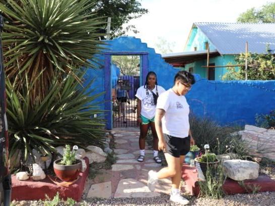 Two students outside, near a blue painted wall and potted flowers