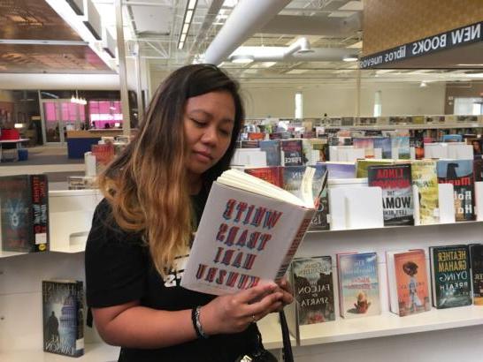 A student in a bookstore reading a book that says "White Tears by Hari Kunzru"