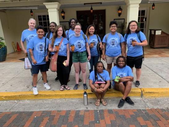 A group of students in matching blue shirts pose in front of a building