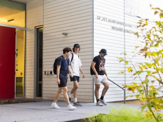 Three students smile as they walk and talk and exit the Campus Ministry building.