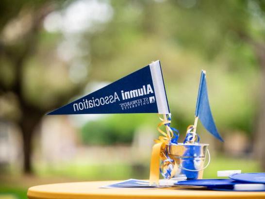 An alumni association mini penant in a smal tin bucket with blue and gold ribbons on a table with a gold tablecloth.