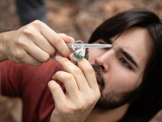 A student holds up a pipette and uses a small magnifying glass to look inside for a specimen. 