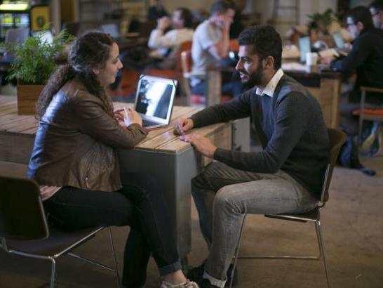 Two students sit across from one another and talk during a networking event at a coffee shop.