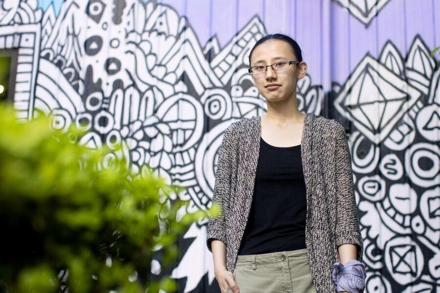 Murphy Chen stands in front of a black, white and purple mural in downtown Austin.