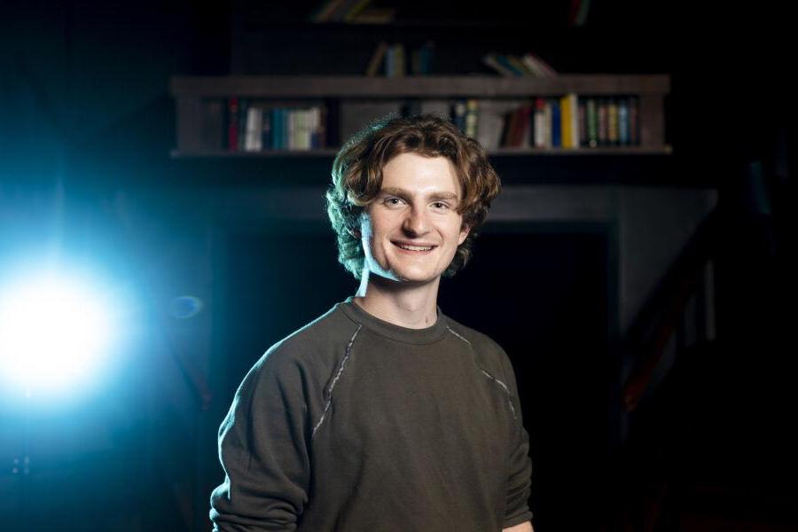 Andrew Mueller stands in the Mary Moody Northern Theatre with a set piece for a play behind him.