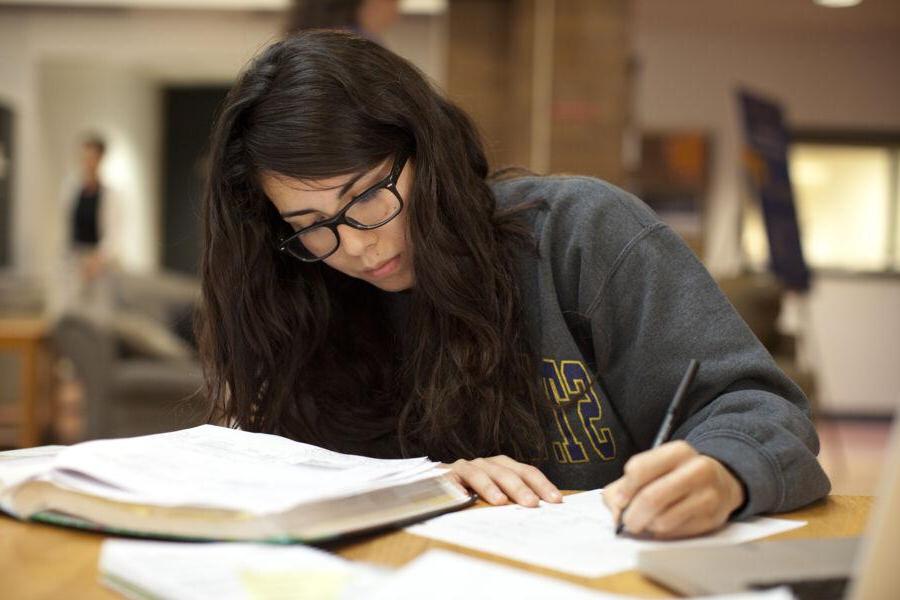 A student with glasses doing homework and reading from a textbook in the library